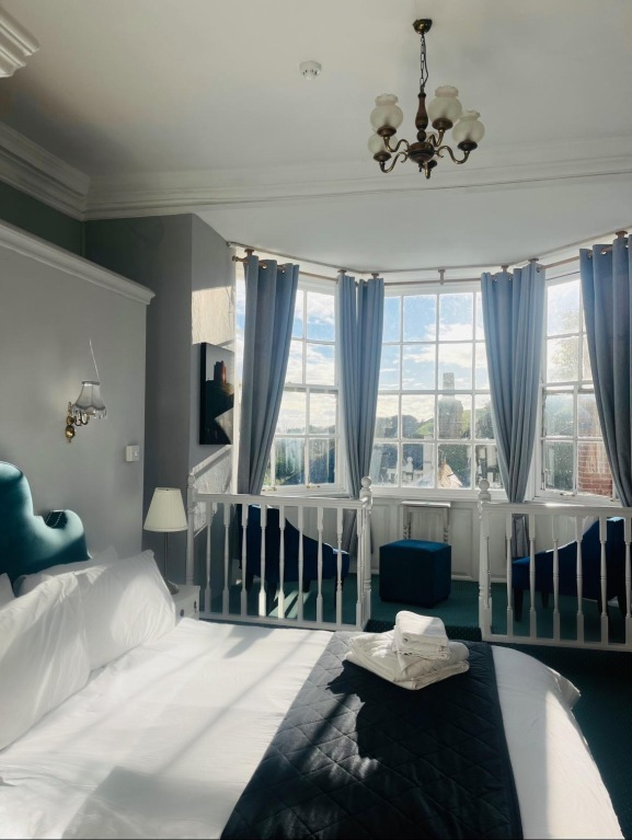 Guest bedroom with white linen bed, bay window and chandelier at The Ilchester Arms
