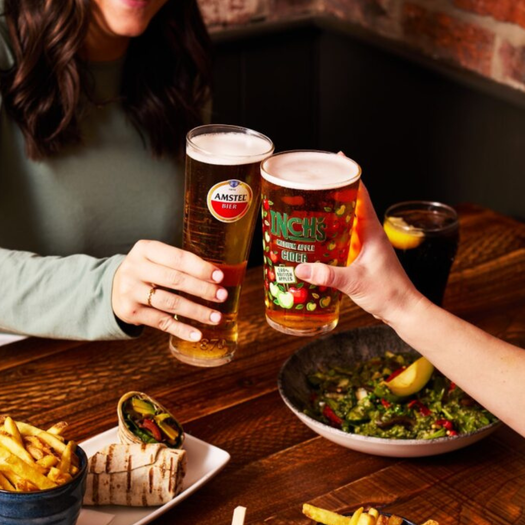 Friends raising a pint and a cider over pub food at The Ilchester Arms